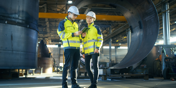 Two young project engineers in a factory discussing a project using a tablet